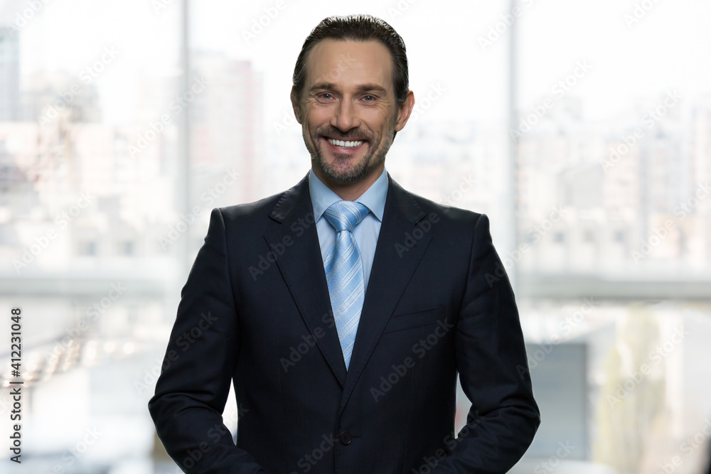 Portrait of smiling mature businessman in office. Huge blurred office windows on the background.