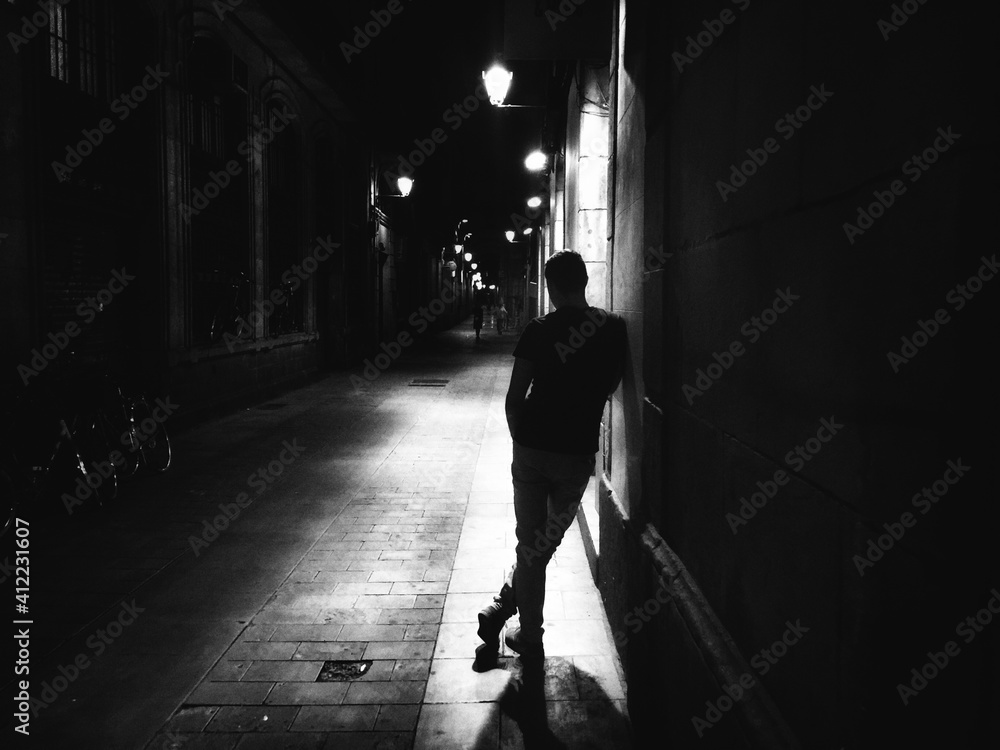 Rear View Of Man Standing By Wall At Night - obrazy, fototapety, plakaty 