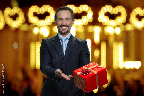 Businessman in suit is presenting big red gift box. Present for christmas. Blurred lighted background. photo