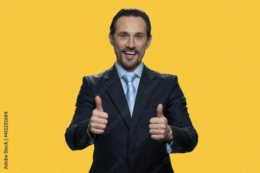 Portrait of businessman shows thumbs up. Confident positive senior manager is showing like gesture as a sign of approval. Isolated on yellow background. Portrait of businessman shows thumbs up. Confident positive senior manager is showing like gesture as a sign of approval. Isolated on yellow background.