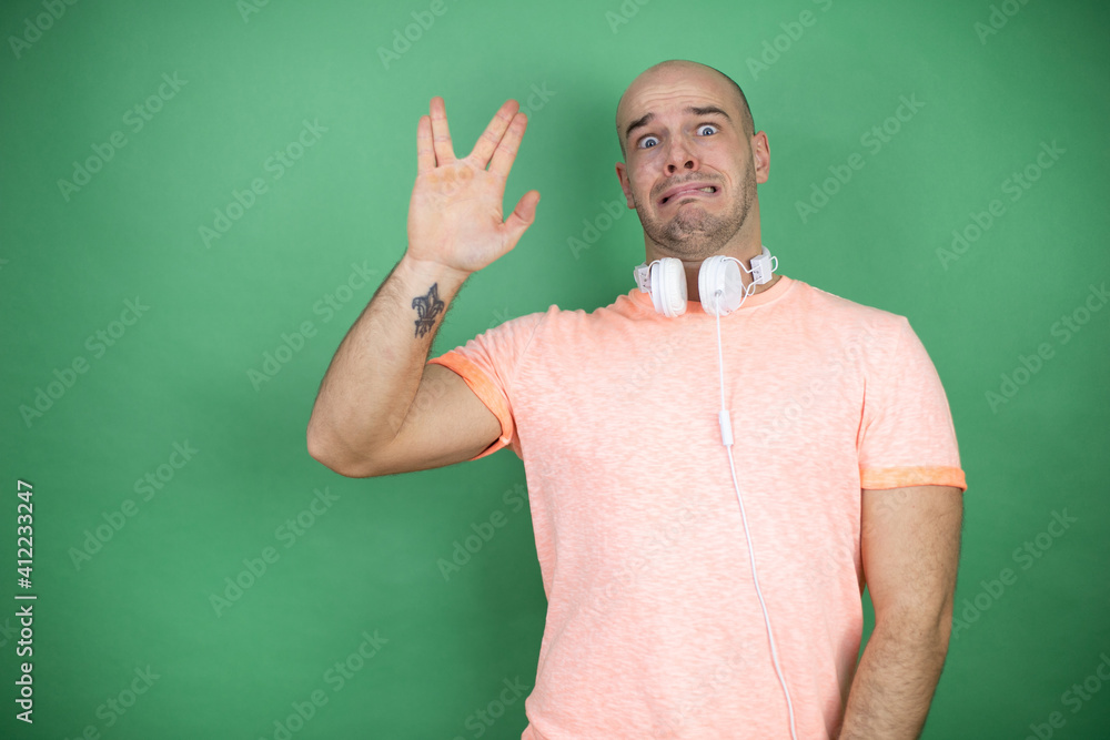 Young bald man using headphones over green background doing star trek freak symbol Young bald man using headphones over green background doing star trek freak symbol