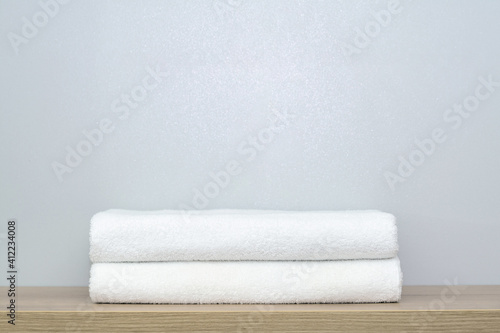 A view of two neatly folded white bath towels on a wooden shelf.
