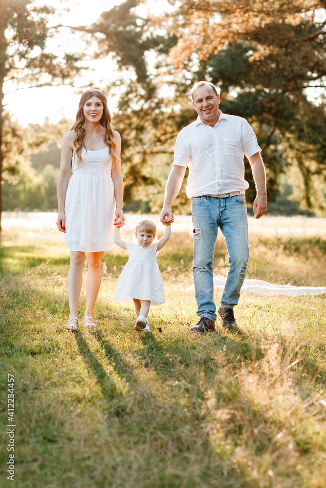 Portrait of happy family. Mom, dad and daughter walk in the park in nature. Young family spending time together on vacation, outdoors. The concept of summer holiday. Mother's, father's, baby's day. Portrait of happy family. Mom, dad and daughter walk in the park in nature. Young family spending time together on vacation, outdoors. The concept of summer holiday. Mother's, father's, baby's day.