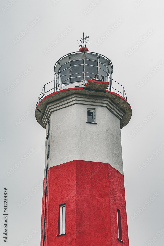 Red and white lighthouse against a gray sky. Oceanfront Tower. High building.