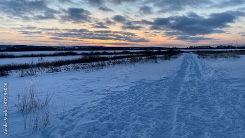 The setting sun illuminates the winter landscape. Dirt road in the snow.
