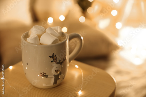 Cup of hot drink with marshmallows on small wooden table  space for text. Christmas atmosphere