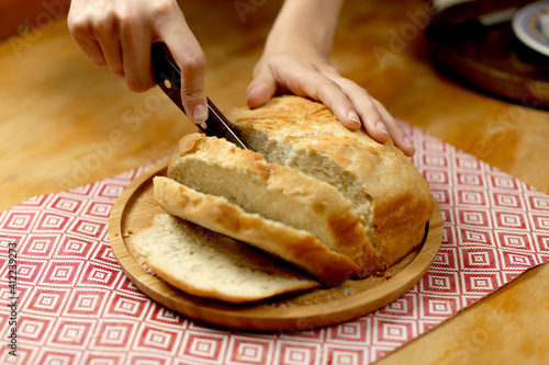 A delicious homemade bread being held and sliced by hands with a knife