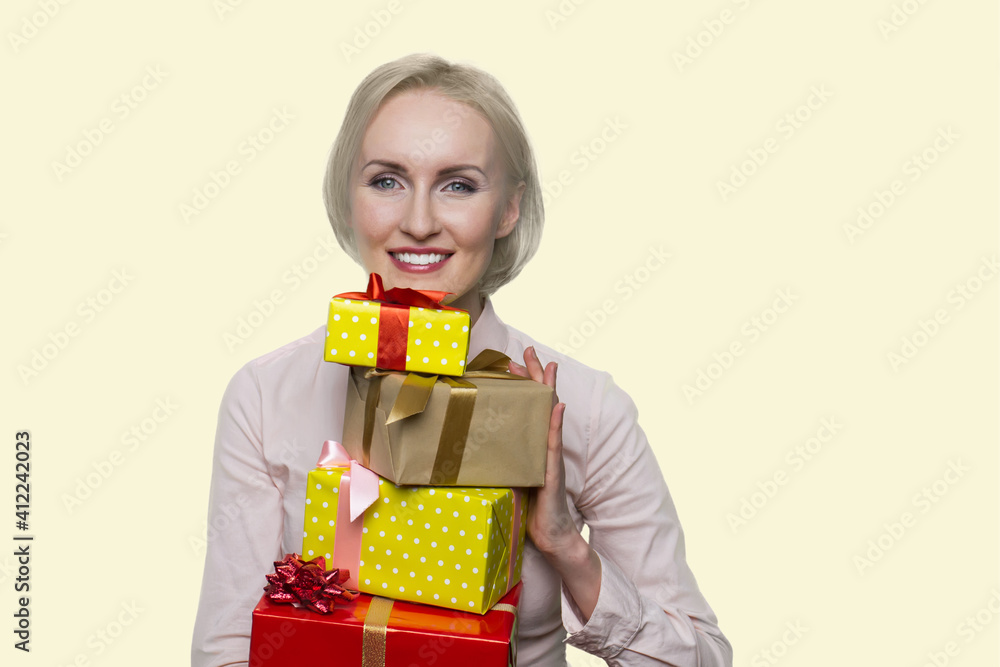 Joyful american woman is holding many gift boxes. Cheerful middle-aged blonde woman isolated on yellow background. Joyful american woman is holding many gift boxes. Cheerful middle-aged blonde woman isolated on yellow background.