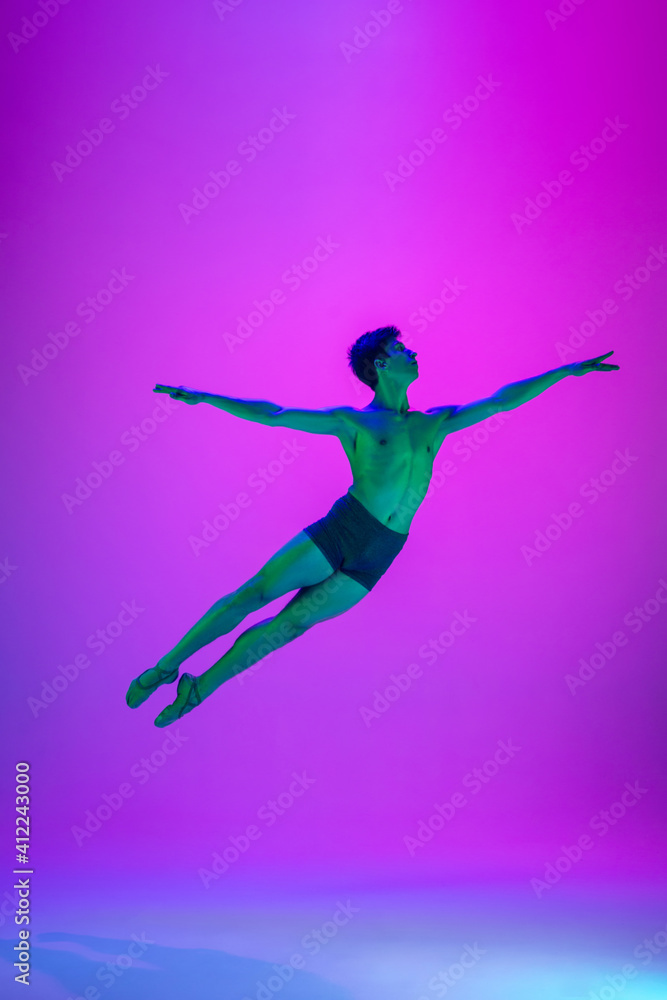 Fototapeta premium Flying. Young and graceful ballet dancer on purple studio background in neon light. Art, motion, action, flexibility, inspiration concept. Flexible caucasian ballet dancer, moves in glow.