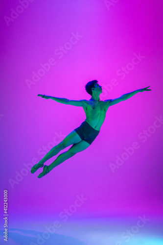 Flying. Young and graceful ballet dancer on purple studio background in neon light. Art  motion  action  flexibility  inspiration concept. Flexible caucasian ballet dancer  moves in glow.