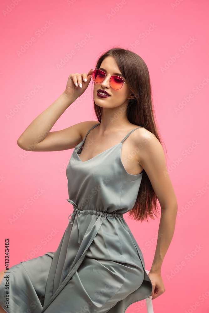 young beautiful fashionable girl in a gray dress and multicolored glasses on a pink background