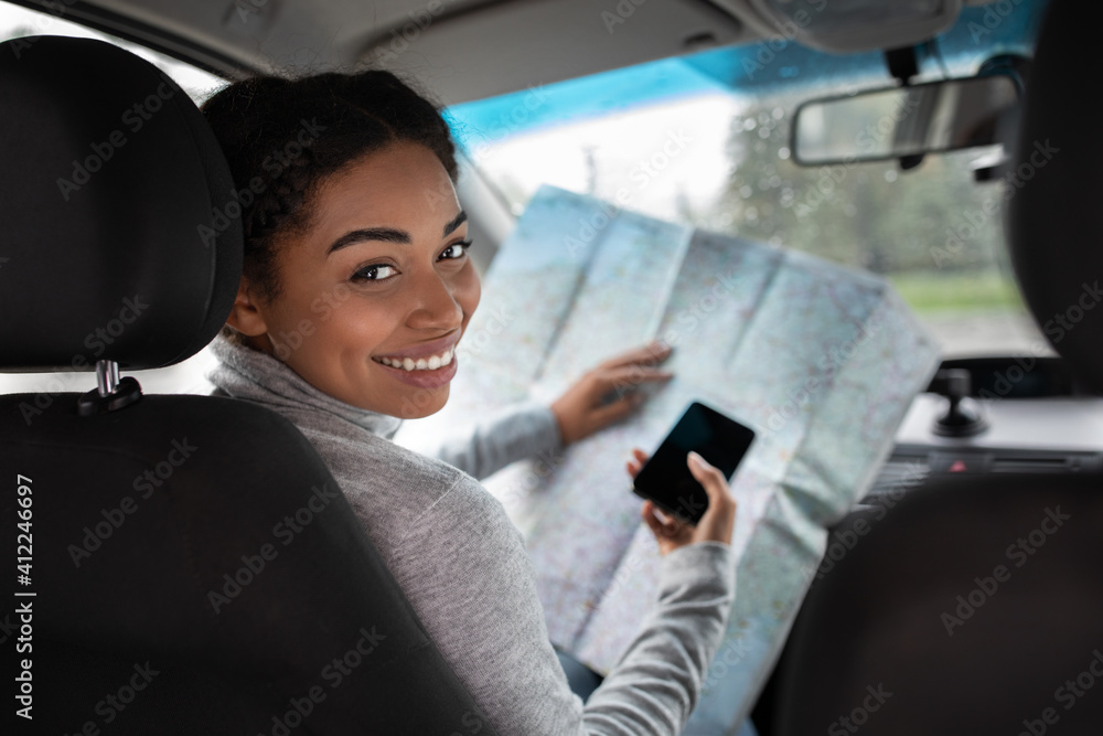 Smiling attractive cute young african american woman driver researching map and holding phone Smiling attractive cute young african american woman driver researching map and holding phone