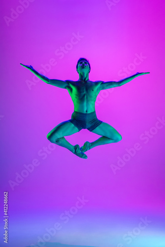 Power. Young and graceful ballet dancer on purple studio background in neon light. Art, motion, action, flexibility, inspiration concept. Flexible caucasian ballet dancer, moves in glow.