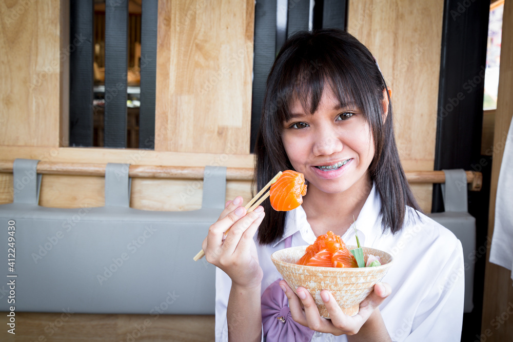 A girl teenage shows a raw salmon uses chopsticks from salmon don in a Japanese restaurant. A girl teenage shows a raw salmon uses chopsticks from salmon don in a Japanese restaurant.