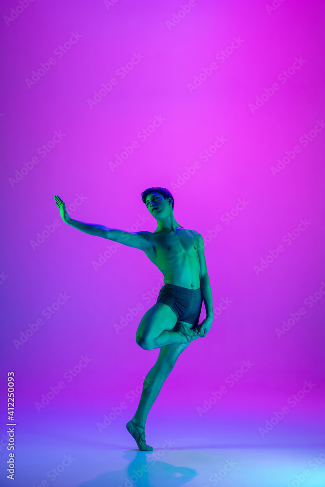 Performing. Young and graceful ballet dancer on purple studio background in neon light. Art, motion, action, flexibility, inspiration concept. Flexible caucasian ballet dancer, moves in glow.
