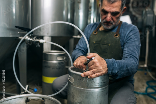 brewer working in his craft beer brewery. top up barrels of beer