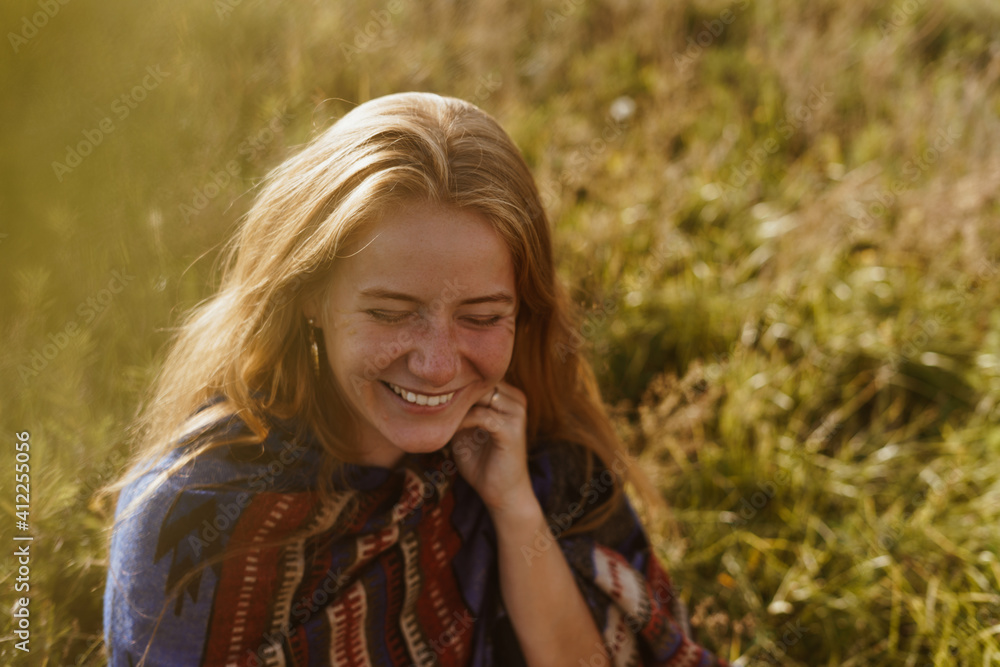 unusually sunny appearance in a red-haired girl with freckles on her face joyfully laughing who sits on the steppe grass. High quality photo