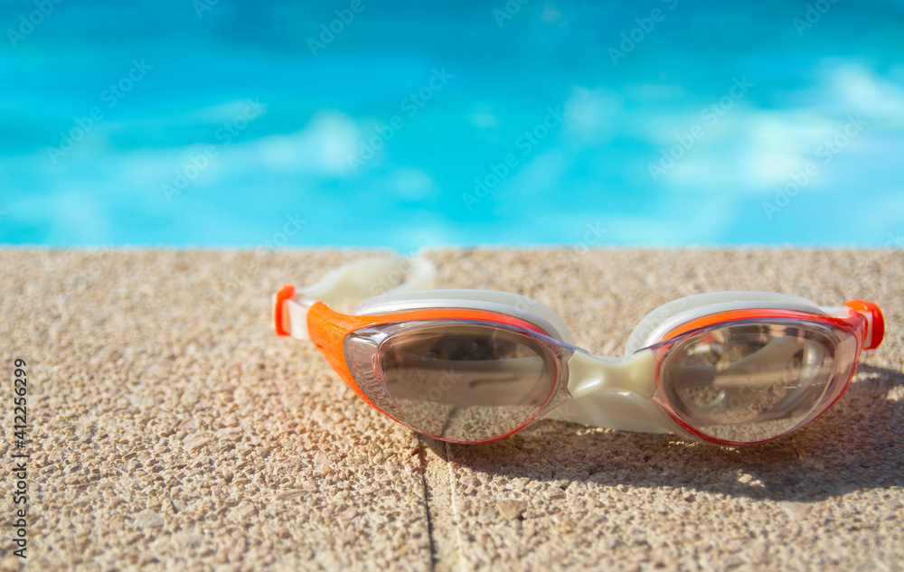 Swimming goggles lie at the edge of the blue pool on a sunny day