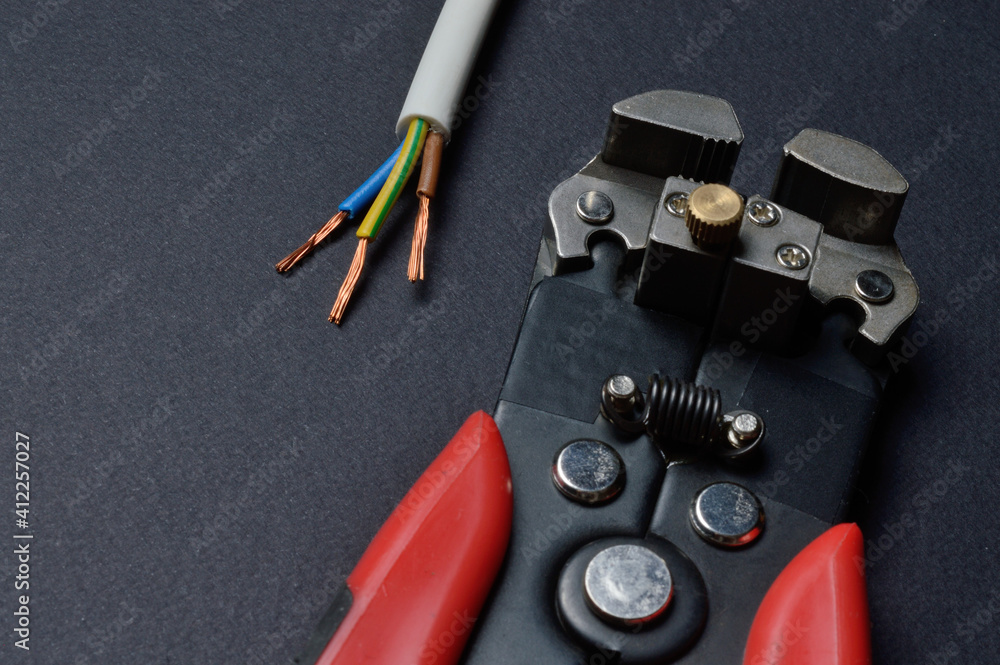 wire cutters and stripped three-core wire. dark background. close-up. wire cutters and stripped three-core wire. dark background. close-up.