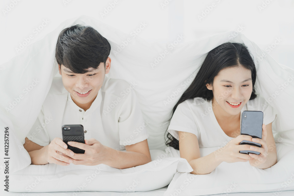 Young couple using phone in bed with cheerful expressions Young couple using phone in bed with cheerful expressions