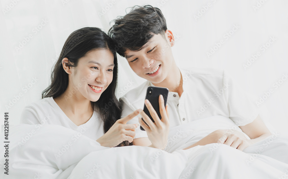 Young couple using phone in bed with cheerful expressions Young couple using phone in bed with cheerful expressions