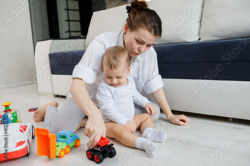 Young mom and little child plays with toys sitting on floor