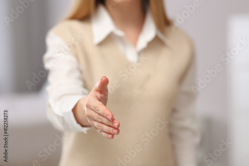 Woman offering handshake indoors, closeup. Space for text