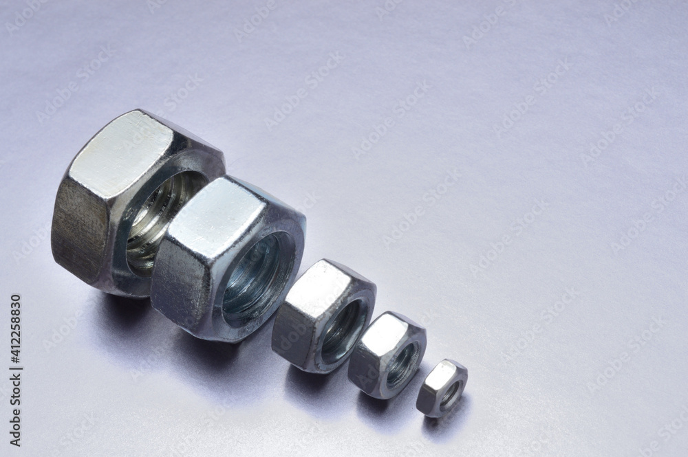 five new chrome nuts of different sizes from large to small are lined up. metallic background. close-up. five new chrome nuts of different sizes from large to small are lined up. metallic background. close-up.