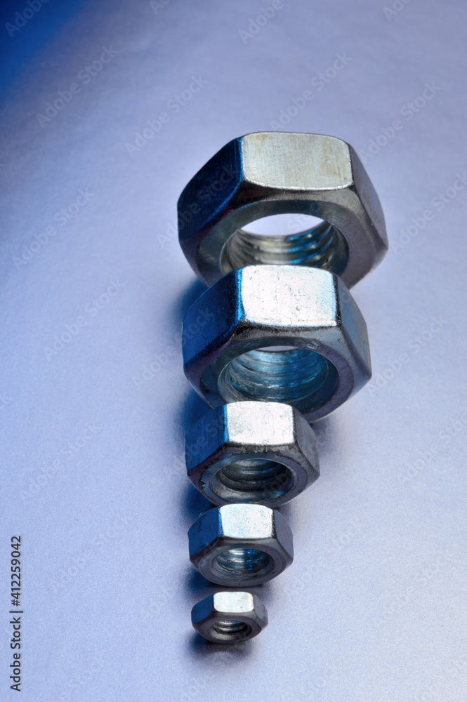 five new chrome nuts of different sizes from large to small are lined up. metallic background. close-up. five new chrome nuts of different sizes from large to small are lined up. metallic background. close-up.