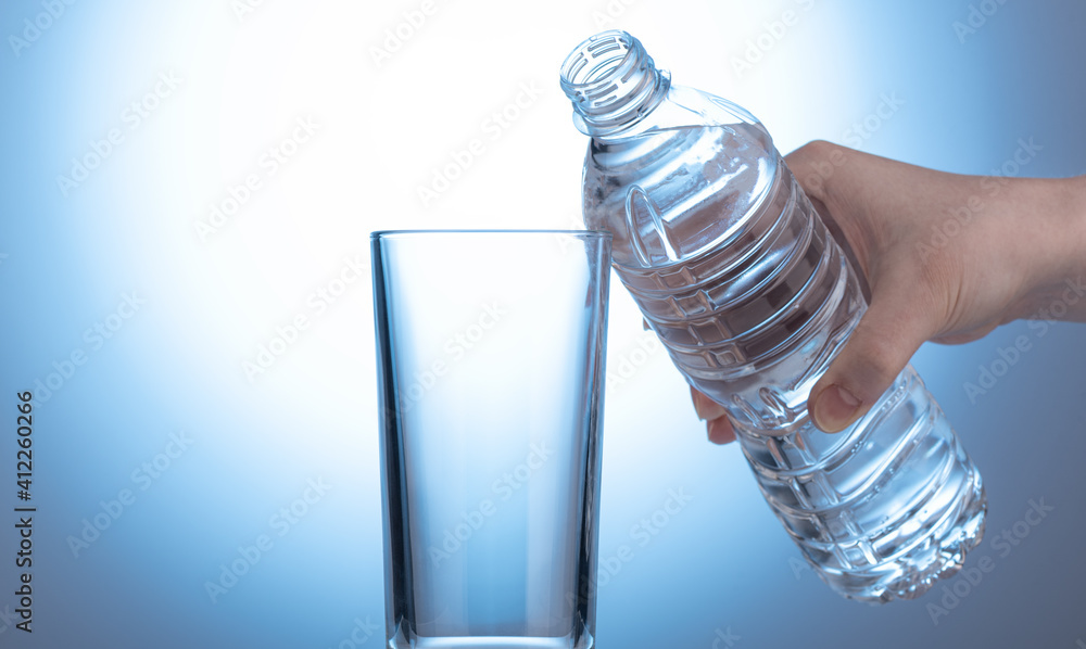 Plastic bottle with water in a female hand. Empty glass beaker. Plastic bottle with water in a female hand. Empty glass beaker.