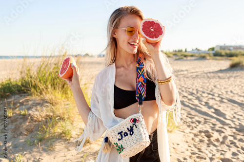 Summer portrait of playful carefree woman posing with tasty grapefruit halves in hands.
