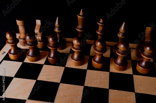 Black wooden pieces on a chessboard. A chessboard set up during a game on a black background
