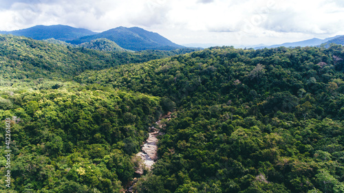 Drone shot aerial view top angle rain forest in Sumbawa, Indonesia. Lush green thick dense woods river bridge mountains bright sunny day beautiful weather valleys terrain nature streams