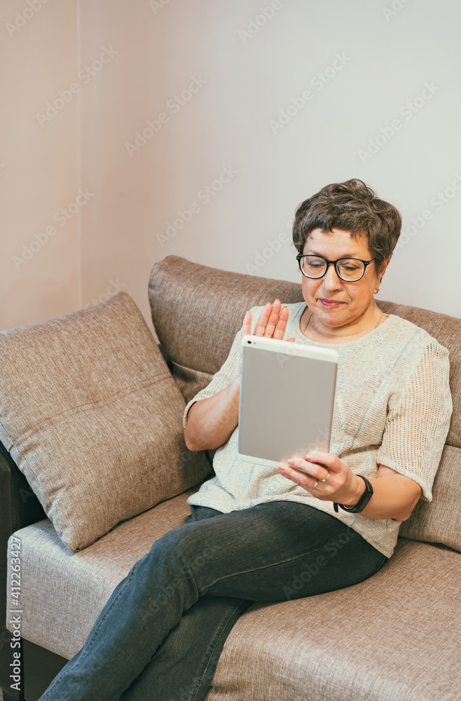 Attractive elegant senior woman sitting on the couch and using a tablet computer at home. Attractive elegant senior woman sitting on the couch and using a tablet computer at home.