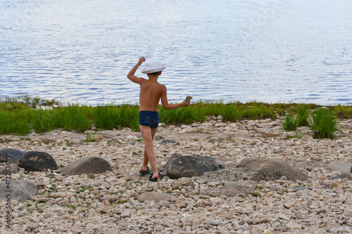 A boy with raised arms walks along a pebble beach