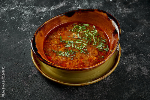 A dish of Georgian cuisine - Kharcho, beef soup with rice, walnuts and tklapi or tkemali sour sauce. Spicy soup on a dark background photo