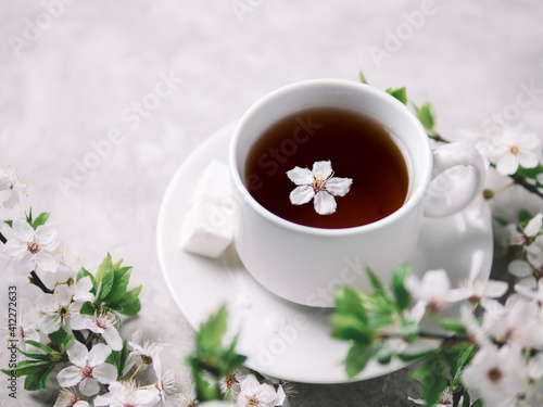 A cup of fragrant tea on a white stone table, branches of cherry blossoms