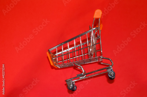 Empty small orange and pink shopping trolley or cart isolated on red background. Shopping concept.
