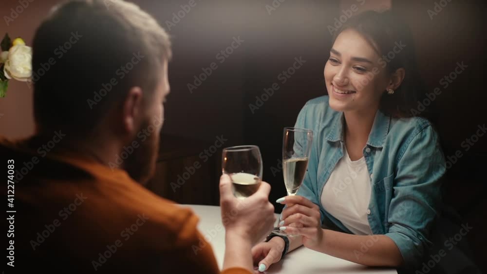 Back view of happy couple of clinking white wine glasses or champagne during romantic dinner. Love couple celebrating anniversary or Valentines day at home. Shooting in slow motion. Back view of happy couple of clinking white wine glasses or champagne during romantic dinner. Love couple celebrating anniversary or Valentines day at home. Shooting in slow motion.