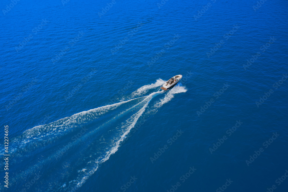 Obraz premium Drone view of a boat sailing at high speed. Aerial view of a boat in motion on blue water. luxury motor boat. Top view of a white boat sailing in the blue sea.