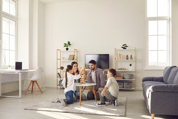 Happy family father mother and two children sitting on floor and playing at home together during weekend. Family spending happy time at home and having fun with children concept