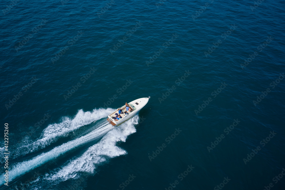 Drone view of a boat sailing across the blue clear waters. Top view of a white boat sailing to the blue sea. Motor boat in the sea. Travel - image. Drone view of a boat sailing across the blue clear waters. Top view of a white boat sailing to the blue sea. Motor boat in the sea. Travel - image.