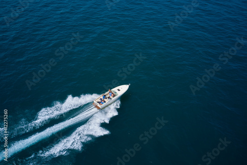 Drone view of a boat sailing across the blue clear waters. Top view of a white boat sailing to the blue sea. Motor boat in the sea. Travel - image. © Berg