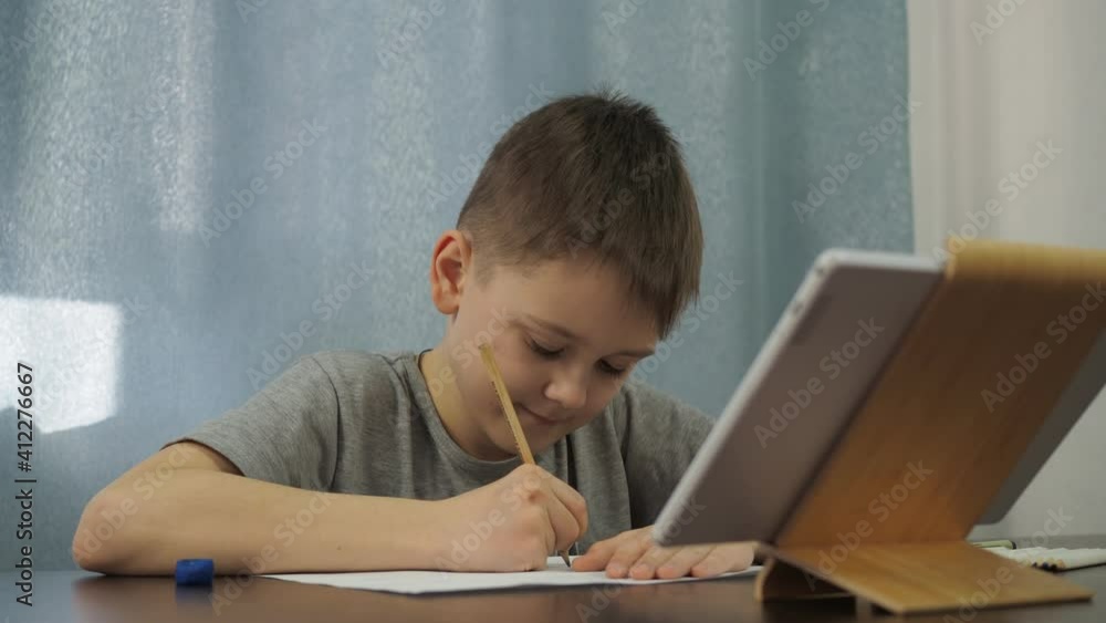 a boy in a gray T-shirt draws a picture with a pencil from a tablet. art lessons online. a boy in a gray T-shirt draws a picture with a pencil from a tablet. art lessons online.