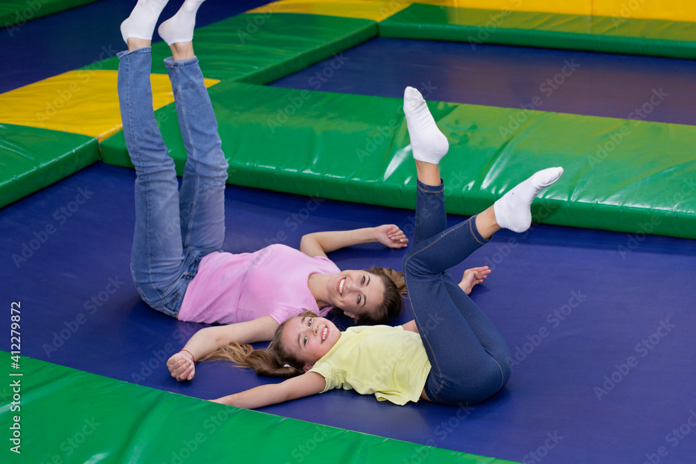 Cute teen girl and her happy mother lying on trampoline, lifting their legs  up, having fun together at amusement park Stock Photo | Adobe Stock