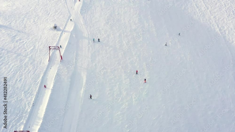 Ski lift elevator transporting skiers and snowboarders on snowy winter slope at mountain resort. Top view from drone chairlift moving on cable way in ski resort. UHD 4k video Ski lift elevator transporting skiers and snowboarders on snowy winter slope at mountain resort. Top view from drone chairlift moving on cable way in ski resort. UHD 4k video