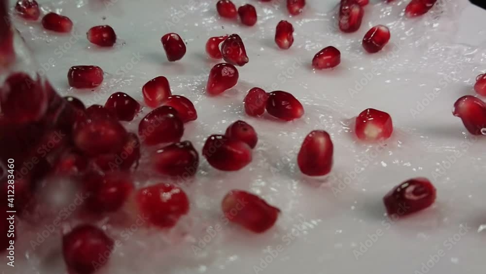 Water is flowing heavily down on the wet surface with juicy red pomegranate grains in slow motion Water is flowing heavily down on the wet surface with juicy red pomegranate grains in slow motion