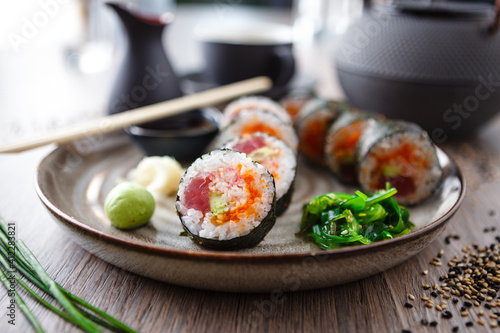 Sushi maki rolls with tuna, flying fish caviar, crab, avocado on a plate with chopsticks, soy sauce, wasabi and ginger. Japanese traditional food closeup served for lunch in modern gourmet restaurant