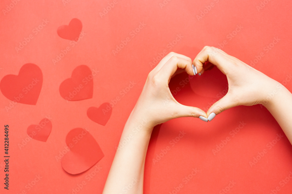 Heart from hands near red hearts decoration on a red background. Red heart decoration. Woman hands making a heart shape on a red isolated background. Valentines Day concept. Charity, donation concept.