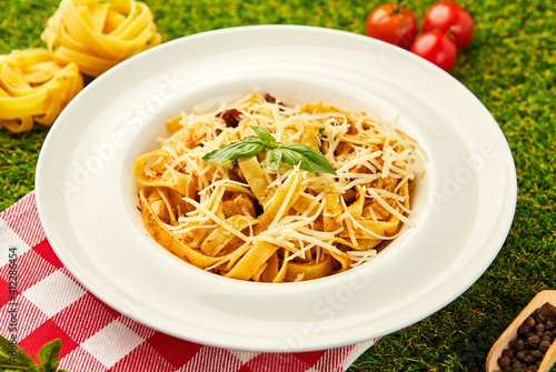 Spaghetti pasta with pesto sauce and sun-dried tomatoes served in a plate with parmesan cheese and basil